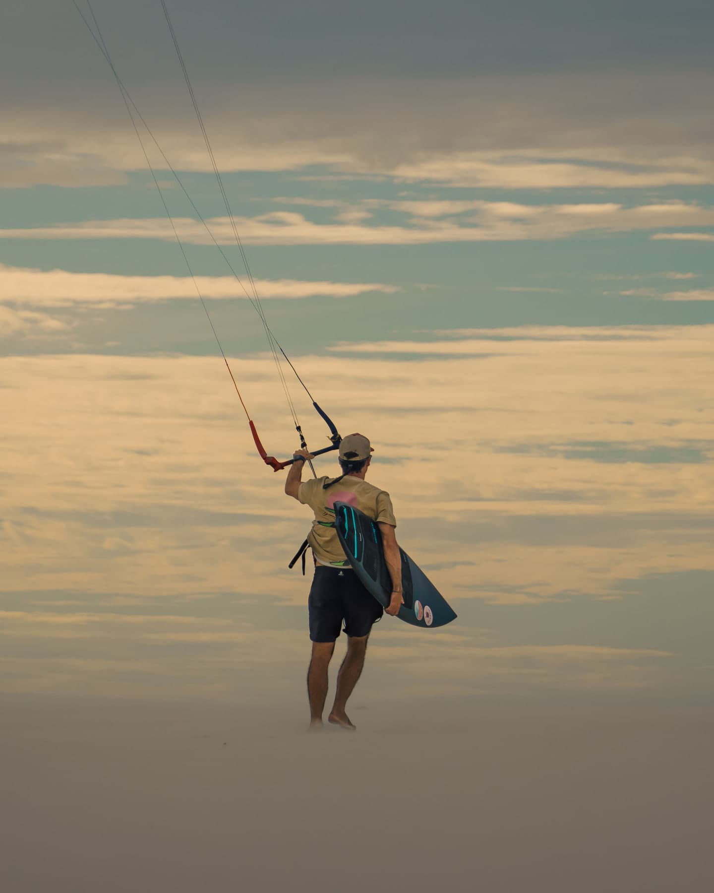 Guilly Brandão na areia, com a prancha e o kite no alto, ao fim do dia
