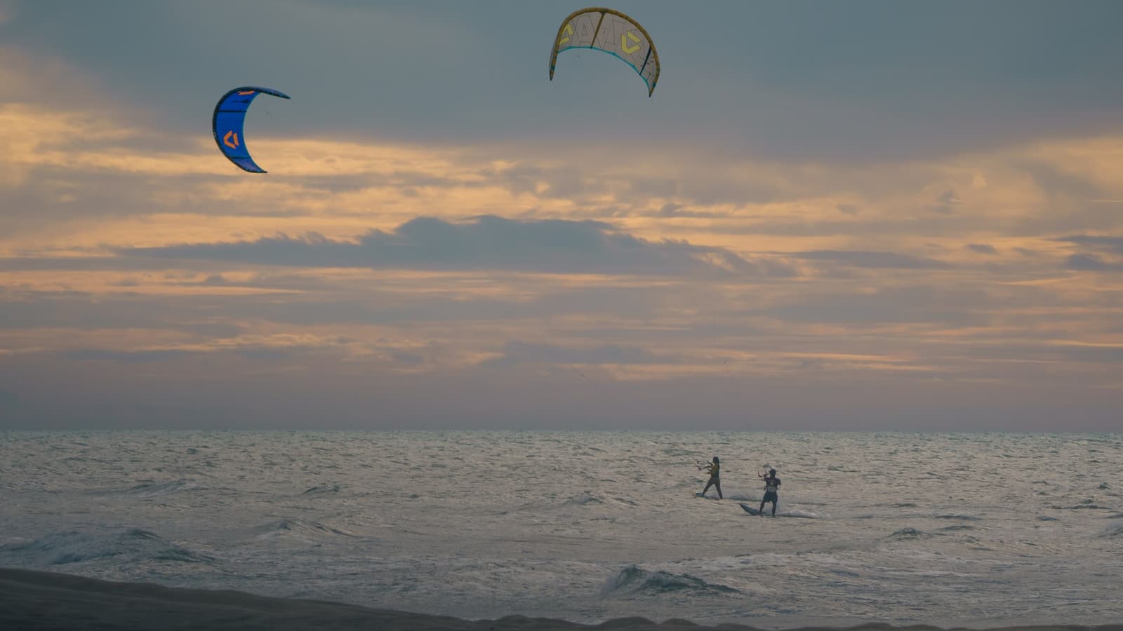 Dois kites num céu aberto, sobre um mar praticamente vazio
