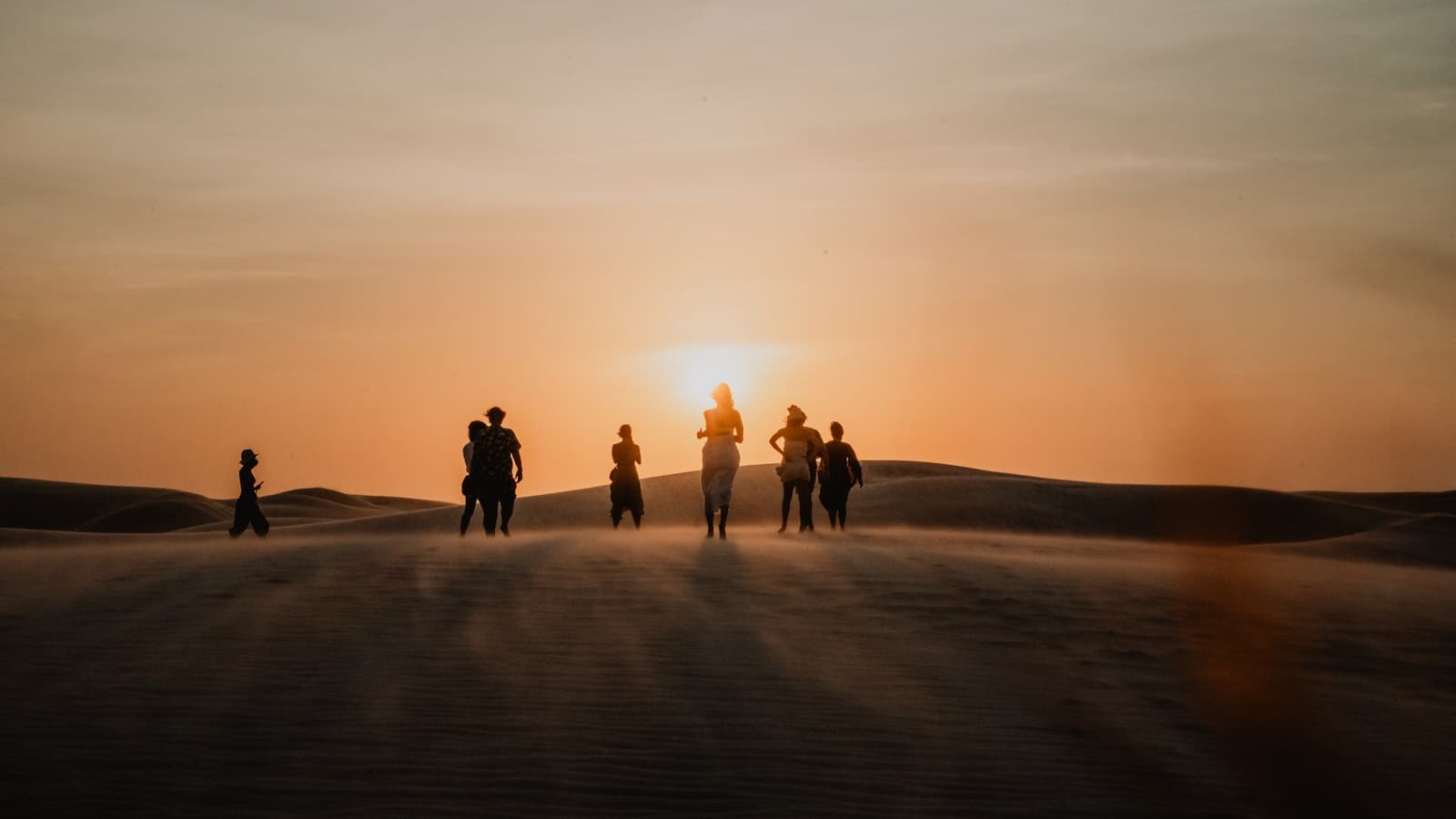 Grupo caminhando na duna, contra o sol baixo